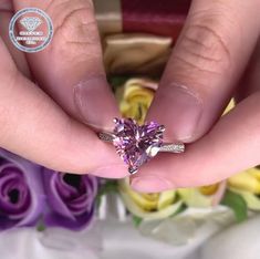 a woman's hands holding a ring with a pink heart shaped diamond on it