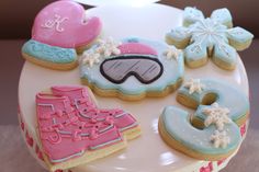 decorated cookies are arranged on top of a white cake platter with snowflakes, mittens, and skis