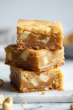 three pieces of peanut butter bars stacked on top of each other with nuts scattered around them