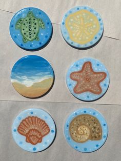 four ceramic coasters with sea animals and seashells painted on them, all in different colors