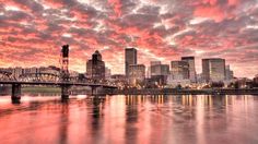 the city skyline is reflected in the water at sunset, with pink and orange clouds