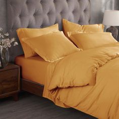 a bed with yellow sheets and pillows in a bedroom next to a lamp on a nightstand