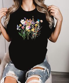 This  colorful wildflower unisex  shirt is perfect for hot summer days. With wildflowers, butterfly and a dragonfly ♥ PRODUCTION TIME: 1-5 days (Usually 2-3 days) ♥ SHIPPING TIME: 2-5 days (Usually 3 days) ♥ PRODUCT DESCRIPTION:   Our Relaxed Fit Tee (Bella + Canvas style 3001) is a unisex style that runs a touch small for men, and about a half a size large for women. It's a relaxed fit and is soft and cozy. * For T-shirt Sizes Please refer to the Listing Image. ♥ CARE INSTRUCTION: Machine wash: Summer Floral Print Crew Neck Shirt, Black Summer Tops With Plant Print, Summer Cotton Shirt With Butterfly Print, Casual Butterfly Print Shirt For Spring, Summer Graphic Tee With Plant Print, Spring Butterfly Print Crew Neck Shirt, Black Botanical Top For Spring, Black Tops With Plant Print For Spring, Botanical Style Shirt With Relaxed Fit For Summer