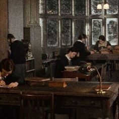 several people sitting at desks in an old fashioned room with books on the table