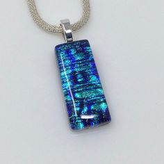 a pendant with blue and green glass in it on a silver chain, sitting on a white surface