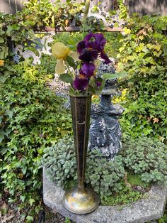 a tall vase with purple flowers sitting on top of a stone slab in a garden