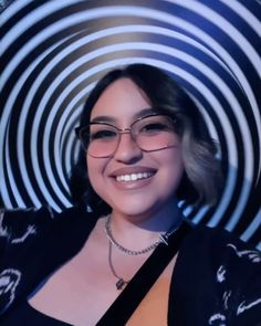 a woman with glasses smiling in front of a black and white circular design wallpaper