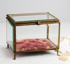 a glass box with red rocks in it and pearls on the floor next to it