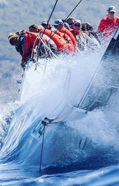 a group of people riding on the back of a sailboat in the middle of a wave