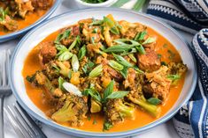 two plates filled with stew and vegetables on top of a white table cloth next to silverware