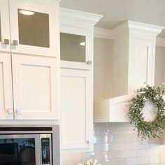 a wreath is hanging on the wall above a microwave in a kitchen with white cabinets