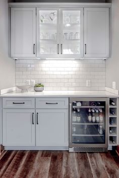 a kitchen with white cabinets and wood flooring is pictured in this image, there is a wine cooler next to the counter