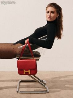 a woman is sitting on a chair with a red purse in front of her legs