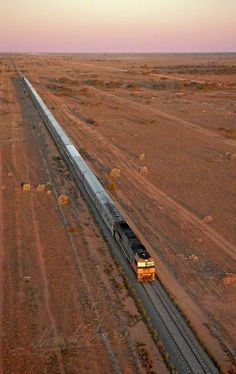 an aerial view of a train on the tracks in the middle of the desert at sunset