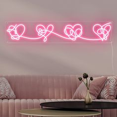 a pink neon sign that says love on the wall above a couch with pillows and a coffee table