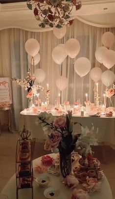 a table topped with lots of white balloons and flowers next to a chandelier