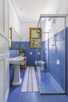 a bathroom with blue walls and flooring has a shower stall, sink, and toilet