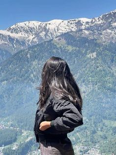 a woman standing on top of a mountain looking at the snow covered mountains in the distance