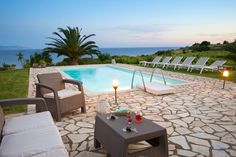 an outdoor patio with lounge chairs and table next to a pool at dusk, overlooking the ocean