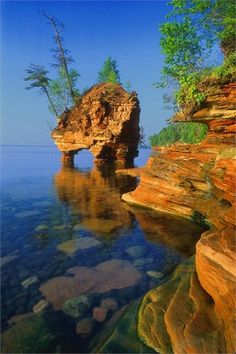 the water is crystal blue and clear with rocks on both sides, and trees in the distance