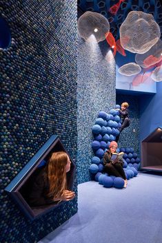 two children are playing in a play room with blue balls and plastic fish on the walls