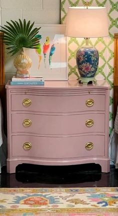 a pink dresser sitting next to a lamp on top of a bed