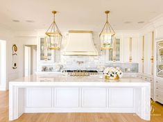 a large kitchen with white cabinets and an island in the middle is surrounded by gold accents