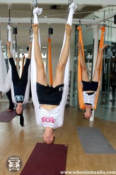 two women doing aerial acrobatic exercises in an indoor gym with yoga mats on the floor