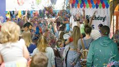 a group of people standing in front of a birthday banner and confetti streamers