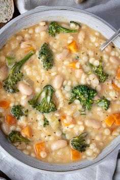 a bowl filled with white beans and broccoli on top of a table next to bread