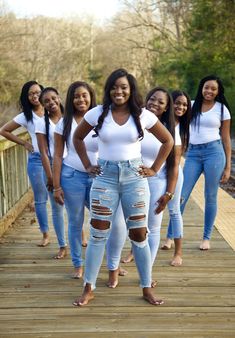 a group of women standing on top of a wooden bridge with their arms around each other