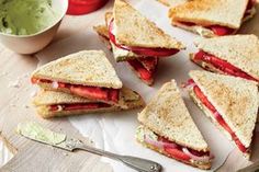 a cut in half sandwich sitting on top of a cutting board next to a bowl of guacamole