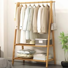 a wooden rack with clothes hanging on it next to a potted plant and bed