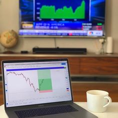 a laptop computer sitting on top of a table next to a coffee cup and television