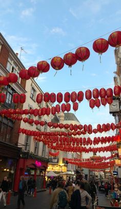 many red lanterns hanging from the side of buildings and people walking down the street in front of them