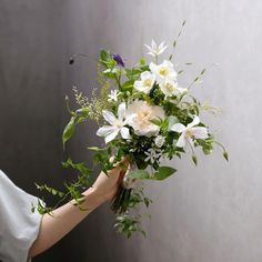 a woman holding a bouquet of flowers in her hand with greenery on the side