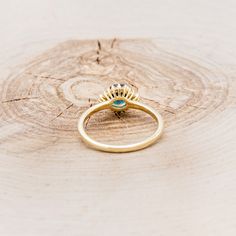 a gold ring sitting on top of a piece of wood with a turquoise stone in the middle