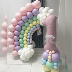 a balloon arch is decorated with pastel balloons and a pink one for the first birthday