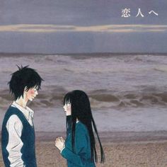 two people are standing on the beach next to the ocean and looking at each other