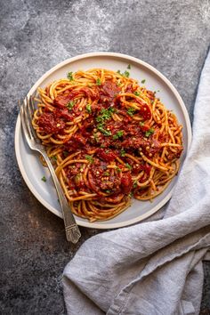 spaghetti with sauce and parsley on a plate next to a fork, napkin and cloth