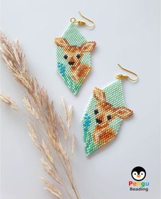 two small beaded fox earrings sitting on top of a white table next to some dry grass