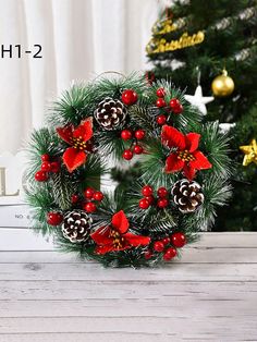 a christmas wreath with poinsettis and pine cones on a table next to a christmas tree