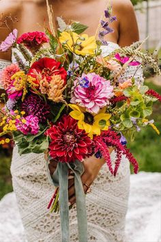 a woman holding a large bouquet of flowers in her hands and wearing a white dress