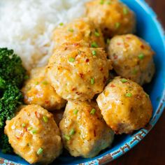 a blue bowl filled with meatballs, broccoli and white rice on top of a wooden table