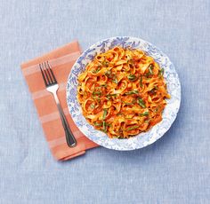 a plate of pasta on a blue and white table cloth with a fork next to it