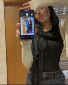 a woman taking a selfie in front of a mirror wearing a white hat and scarf