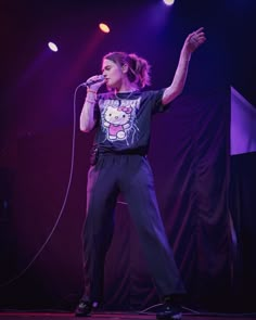 a woman standing on top of a stage holding a microphone in her hand and wearing a hello kitty t - shirt