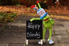 the kermie frog is holding a happy birthday hat and standing next to a sign