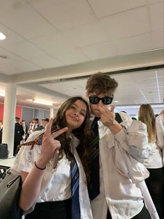 two people standing next to each other at an airport posing for the camera with their fingers in the air