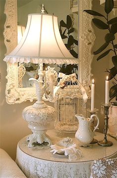 a white table topped with a lamp next to a birdcage filled with birds